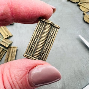 Op de afbeelding: Een close-up van een gouden metalen decoratieve trim met een textuurontwerp. De trim is rechthoekig en heeft een verhoogd middengedeelte.