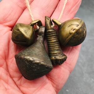 K&ouml;nnte beinhalten: Ein Satz von vier antiken Messingglocken, darunter eine kegelf&ouml;rmige Glocke, eine runde Glocke und zwei kleinere Glocken mit einem dekorativen Design. Die Glocken sind mit einer Schnur zusammengebunden.