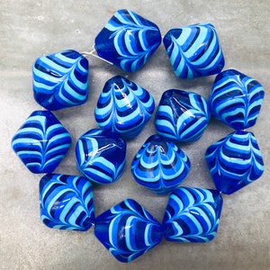 May include: A collection of 12 blue and white glass beads with a marbled swirl pattern. The beads are shaped like a diamond with rounded edges.