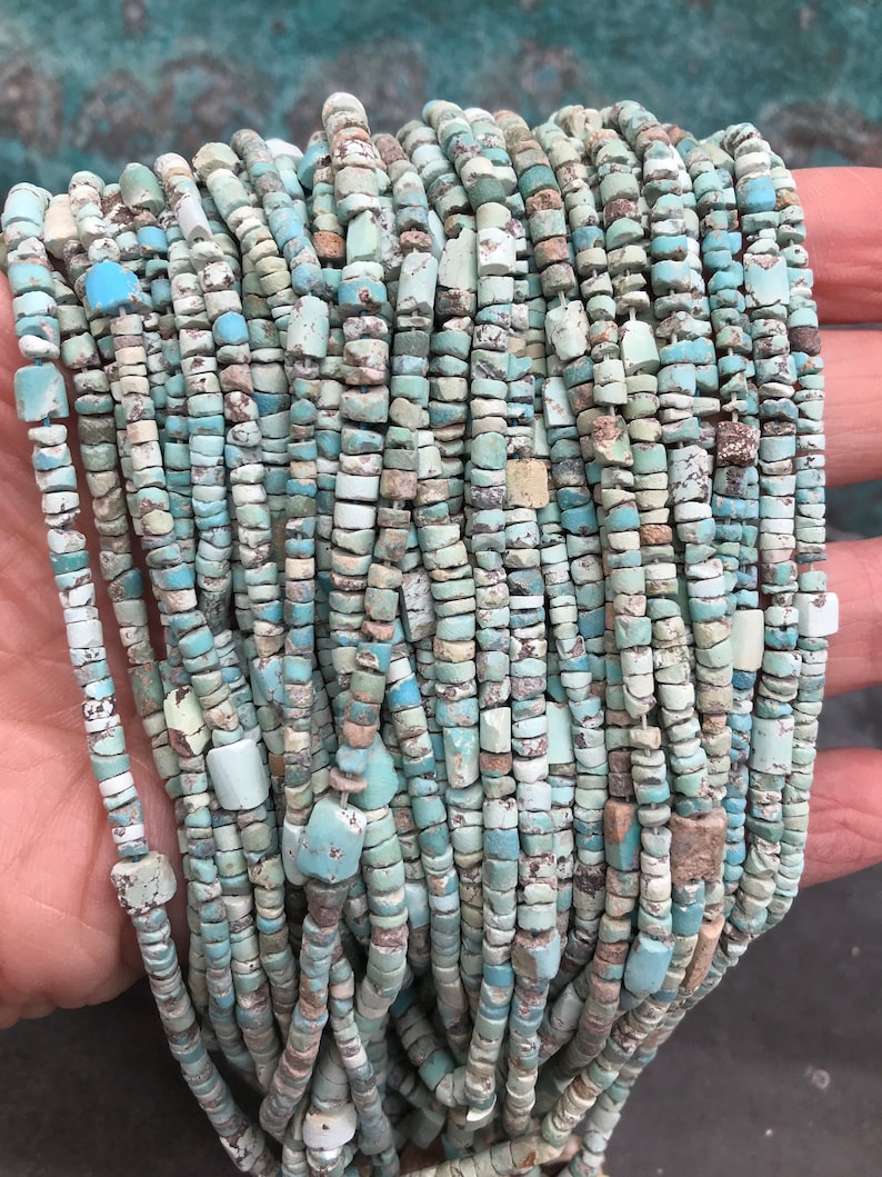 K&ouml;nnte beinhalten: Eine Str&auml;hne aus T&uuml;rkisperlen mit einem Mix aus hell- und dunkelblauen T&ouml;nen und einer rauen, unregelm&auml;&szlig;igen Textur. Die Perlen sind klein und gleichm&auml;&szlig;ig gro&szlig; und auf einer durchsichtigen Schnur aufgef&auml;delt.