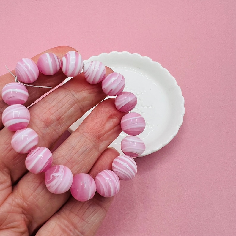 May include: A strand of pink and white striped beads, strung together to form a bracelet. The beads are round and have a glossy finish.