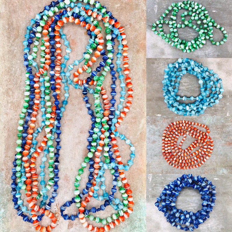 May include: A multi-strand necklace made of colorful paper beads. The beads are striped in shades of blue, green, orange, and white. The necklace is displayed on a textured surface.