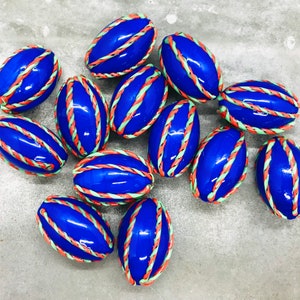 Op de afbeelding: Een groep van 12 blauwe ovale kralen met witte, groene en oranje strepen. De kralen liggen op een grijs oppervlak.