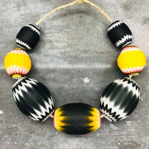 May include: A necklace made of black and white striped glass beads with yellow and pink accents.