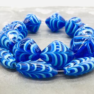 May include: A strand of blue and white glass beads with a swirling pattern. The beads are oval and teardrop shaped.