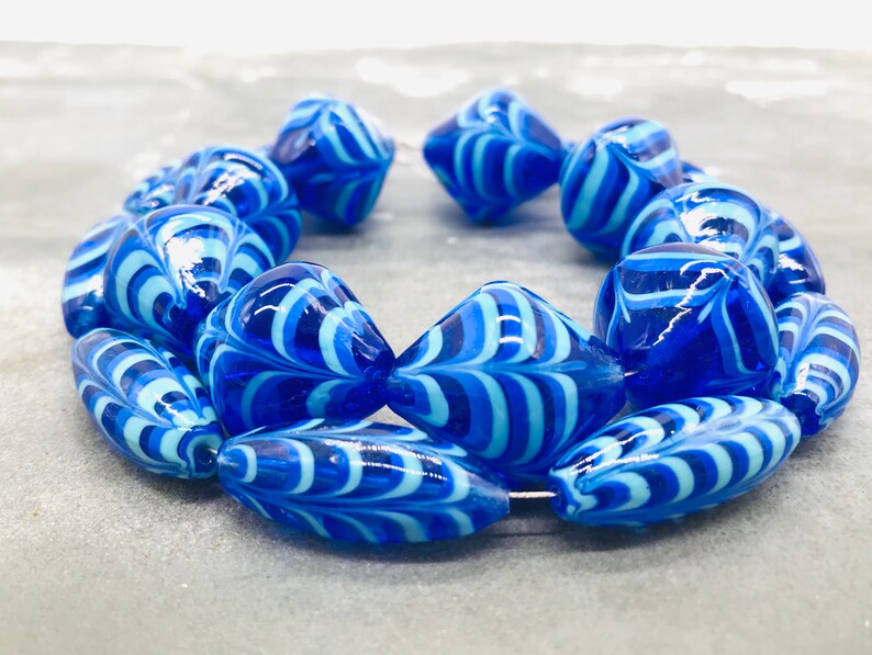 May include: A strand of blue and white glass beads with a swirling pattern. The beads are oval and teardrop shaped.