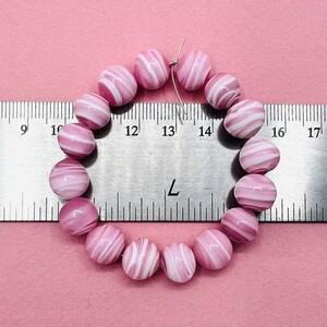 May include: A strand of pink and white striped glass beads, measured against a ruler. The beads are approximately 1 inch in diameter.