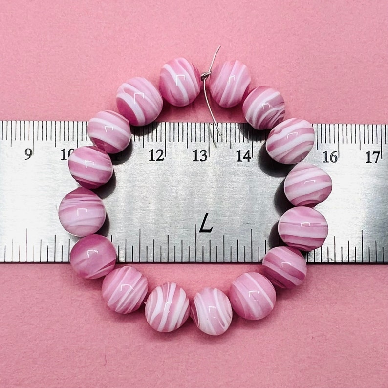 May include: A strand of pink and white striped glass beads, measured against a ruler. The beads are approximately 1 inch in diameter.