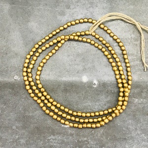 Pu&ograve; includere: Un filo di perline rotonde dorate, infilate su un cordoncino bianco sottile.