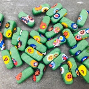 May include: A collection of green glass beads with colorful patterns. The beads are rectangular and have a variety of designs, including flowers, dots, and swirls.