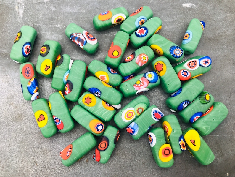 May include: A collection of green glass beads with colorful patterns. The beads are rectangular and have a variety of designs, including flowers, dots, and swirls.