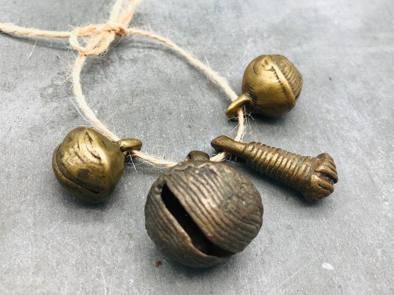 K&ouml;nnte beinhalten: Ein Satz aus vier antiken Messingglocken und einem kleinen Messing-Anh&auml;nger, die mit einer Schnur zusammengebunden sind. Die Glocken haben verschiedene Formen und Gr&ouml;&szlig;en und eine strukturierte Oberfl&auml;che.