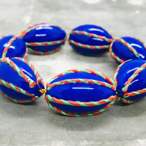 Op de afbeelding: Een armband gemaakt van ovale kralen met een blauwe basis en een ontwerp van groene en oranje strepen.