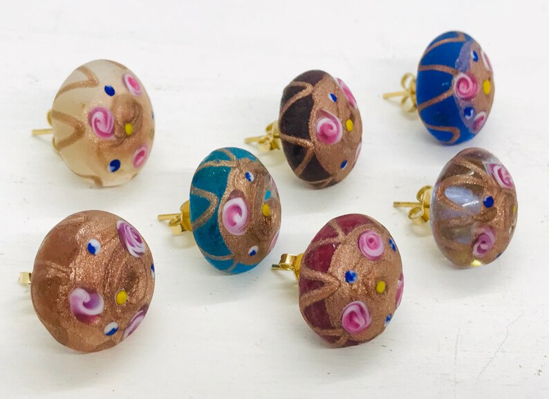 May include: Six pairs of colorful glass earrings with gold accents and floral designs. The earrings are round and have a textured surface.