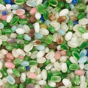 Pu&ograve; includere: Un vasto assortimento di perline di vetro ovali in vari colori, tra cui verde, bianco, blu e rosa. Le perline hanno un aspetto traslucido, leggermente opaco.