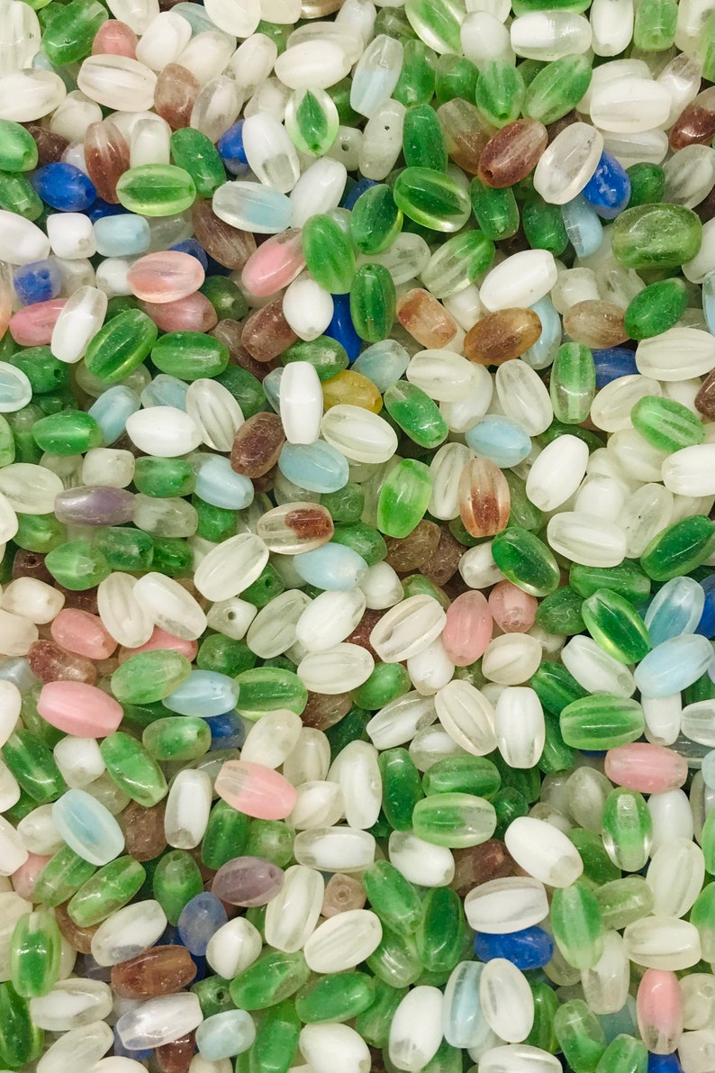 Pu&ograve; includere: Un vasto assortimento di perline di vetro ovali in vari colori, tra cui verde, bianco, blu e rosa. Le perline hanno un aspetto traslucido, leggermente opaco.