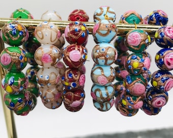 May include: A set of six colorful glass bead bracelets with floral and gold accents. Each bracelet features a different color base with intricate designs.