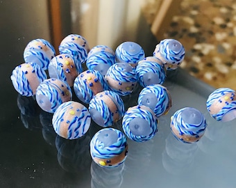 May include: A collection of small, round, glass beads with a blue and white swirl pattern and yellow accents. The beads are translucent and have a slightly iridescent finish.