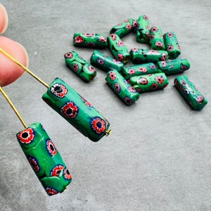 Peut inclure: Un ensemble de perles en verre vertes et rouges avec un motif floral. Les perles sont cylindriques et ont une finition brillante.