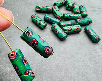 Puede incluir: Una colección de cuentas de vidrio verde y rojo con un patrón floral. Las cuentas son cilíndricas y tienen un acabado brillante.