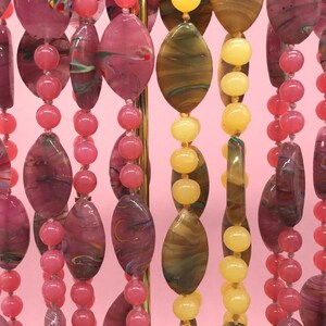 K&ouml;nnte beinhalten: Nahaufnahme von drei Str&auml;ngen bunter Glasperlen. Die Perlen sind oval geformt und haben eine marmorierte Optik. Die Perlen sind auf einem goldfarbenen Draht aufgef&auml;delt.