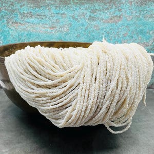 May include: A large bowl filled with white seed beads. The beads are small and round, and they are arranged in a neat pile.