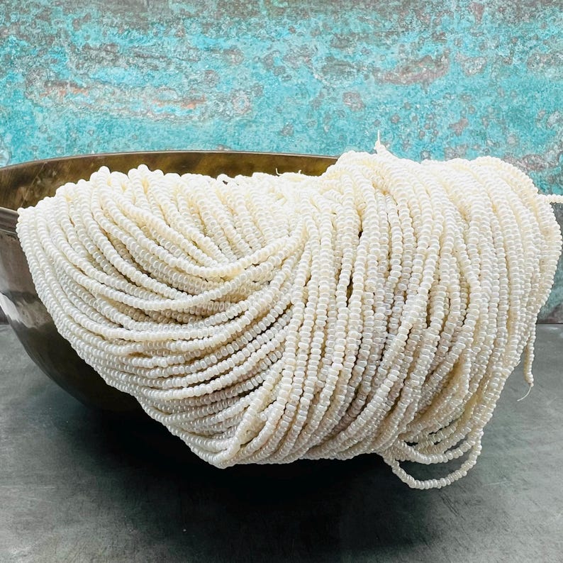 May include: A large bowl filled with white seed beads. The beads are small and round, and they are arranged in a neat pile.