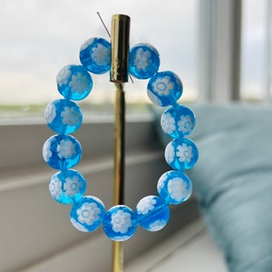 May include: A blue beaded bracelet with white flower designs on each bead.