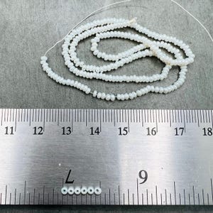 May include: A strand of white seed beads, approximately 14 inches long, is shown next to a ruler. The beads are 11/0 size, which is about 2.2 mm in diameter.  The beads are strung on a thin wire.