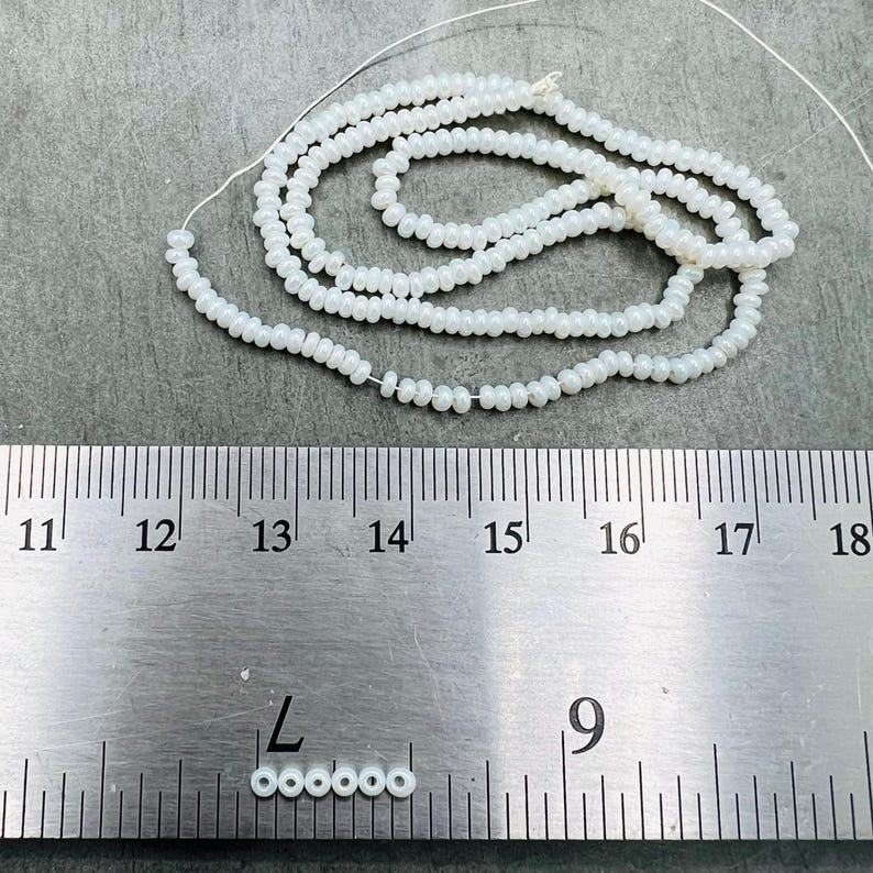 May include: A strand of white seed beads, approximately 14 inches long, is shown next to a ruler. The beads are 11/0 size, which is about 2.2 mm in diameter.  The beads are strung on a thin wire.