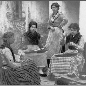 May include: Four women are sitting in a room, three of them are wearing traditional clothing. The woman on the left is wearing a black and white striped dress, the woman in the middle is wearing a black and white checkered dress, and the woman on the right is wearing a black and white checkered dress. The woman in the back is wearing a white dress with a black belt.