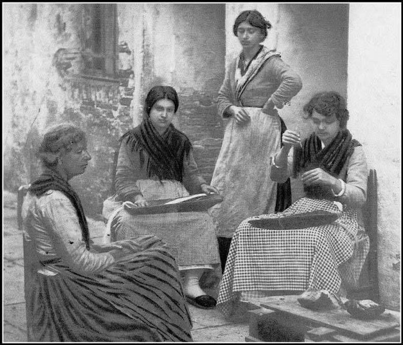 May include: Four women are sitting in a room, three of them are wearing traditional clothing. The woman on the left is wearing a black and white striped dress, the woman in the middle is wearing a black and white checkered dress, and the woman on the right is wearing a black and white checkered dress. The woman in the back is wearing a white dress with a black belt.