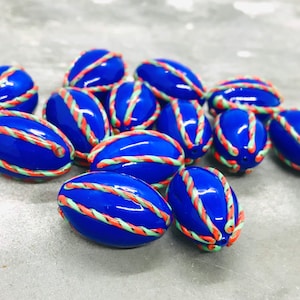 Op de afbeelding: Een groep blauwe, ovale kralen met witte en oranje strepen. De kralen zijn glanzend en hebben een glad oppervlak.