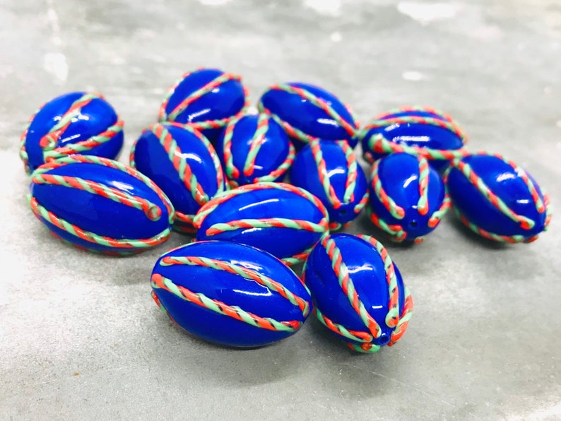 Op de afbeelding: Een groep blauwe, ovale kralen met witte en oranje strepen. De kralen zijn glanzend en hebben een glad oppervlak.