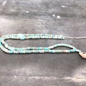 K&ouml;nnte beinhalten: Eine t&uuml;rkisfarbene Perlenkette mit einem Muschelanh&auml;nger. Die Perlen sind eine Mischung aus hell- und dunkelblau.