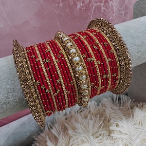 Peut inclure: Un ensemble de bracelets rouges et dorés avec des accents de perles et de strass. Les bracelets sont empilés les uns sur les autres et disposés en forme circulaire.