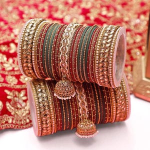 Pode incluir: Um conjunto de pulseiras ornamentadas em tons de vermelho, verde e dourado. As pulseiras são adornadas com detalhes intrincados, incluindo pérolas e enfeites brilhantes. Cada conjunto de pulseiras apresenta um pingente pendurado em forma de sino.