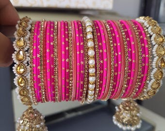 Op de afbeelding: Een stapel roze armbanden met gouden en parelaccenten. De armbanden zijn versierd met gouden versieringen en kleine gouden stippen. De set bevat een met parels bezette armband en bungelende gouden en parelbedels.