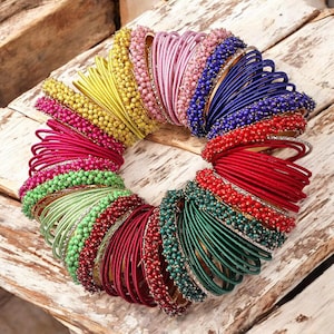 Puede incluir: Un conjunto de pulseras coloridas con detalles de cuentas. Las pulseras están hechas de hilo de seda y están dispuestas en círculo. Los colores incluyen amarillo, rosa, azul, rojo, verde y dorado.