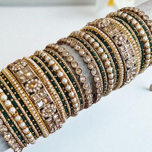 以下が含まれることがあります： 精巧なデザインのゴールドトーンのバングル。エメラルドグリーンの生地を使用したものや、イミテーションパールと透明な宝石で飾られたものがあります。バングルは白い表面に展示されています。