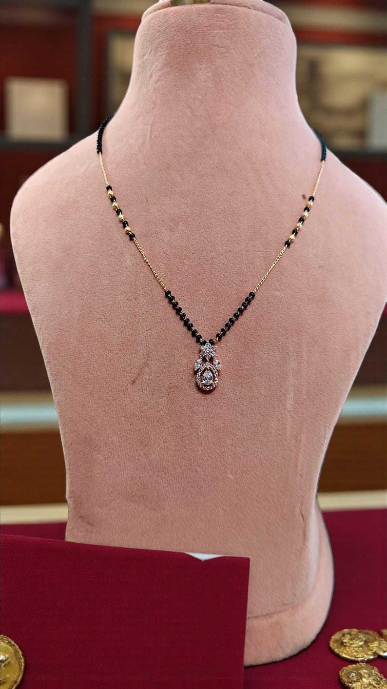 Puede incluir: Un collar de oro con un colgante de diamantes. El colgante tiene un grupo de diamantes y un diamante en forma de l&aacute;grima. El collar tiene una cadena de cuentas negras con detalles dorados.