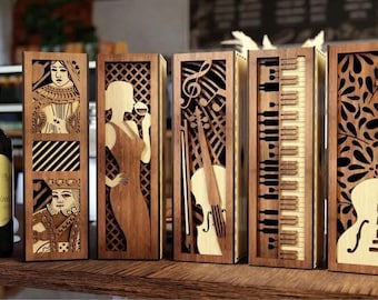 Puede incluir: Cajas de botellas de vino de madera con recortes decorativos. Los diseños incluyen una mujer con una copa de vino, notas musicales y un violín, un teclado de piano y una guitarra. Una botella de vino con tapón dorado está junto a las cajas.