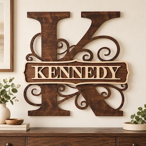 May include: A large, dark brown wooden wall sign featuring a cutout letter K with intricate scrollwork details. A horizontal, light-colored wooden plaque is layered across the center, displaying the name KENNEDY in bold, capital letters.