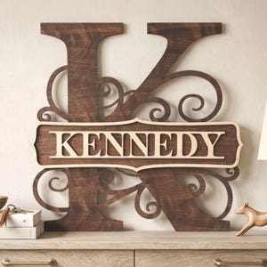 May include: Wooden wall art featuring the letter "K" with the name "KENNEDY" in a light wood color. The dark brown letter has decorative swirls. The name is in a light wood color. This personalized piece is a decorative home accent.