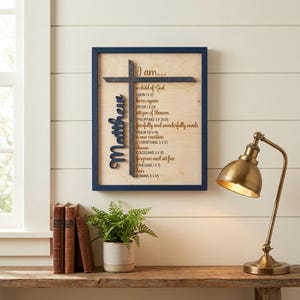 May include: A rectangular wall sign with a dark blue frame and a light wood background. It features a dark cross, the name Matthew in script, and the text I am... followed by a list of religious phrases and Bible verses in dark lettering.