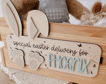 Peut inclure: Une pancarte en bois avec des oreilles de lapin et des empreintes de pattes, indiquant "special easter delivery for PHOENIX".