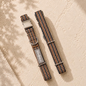May include: Two pet collars featuring a brown, black, and white plaid pattern. Each collar includes silver-toned metal hardware, including a side-release buckle and D-ring. A grey rectangular fabric tag with the text WoofFrills is attached to one.