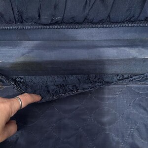 May include: Close-up of a vintage navy blue suitcase interior. The interior features a quilted pattern on the bottom section and a pleated fabric detail at the top. The lining shows signs of wear and age.