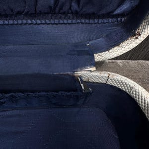 May include: An open, vintage suitcase interior. The interior is navy blue with a quilted pattern. The edges are white with a woven texture. The suitcase appears to be worn, with some fraying and wear visible.