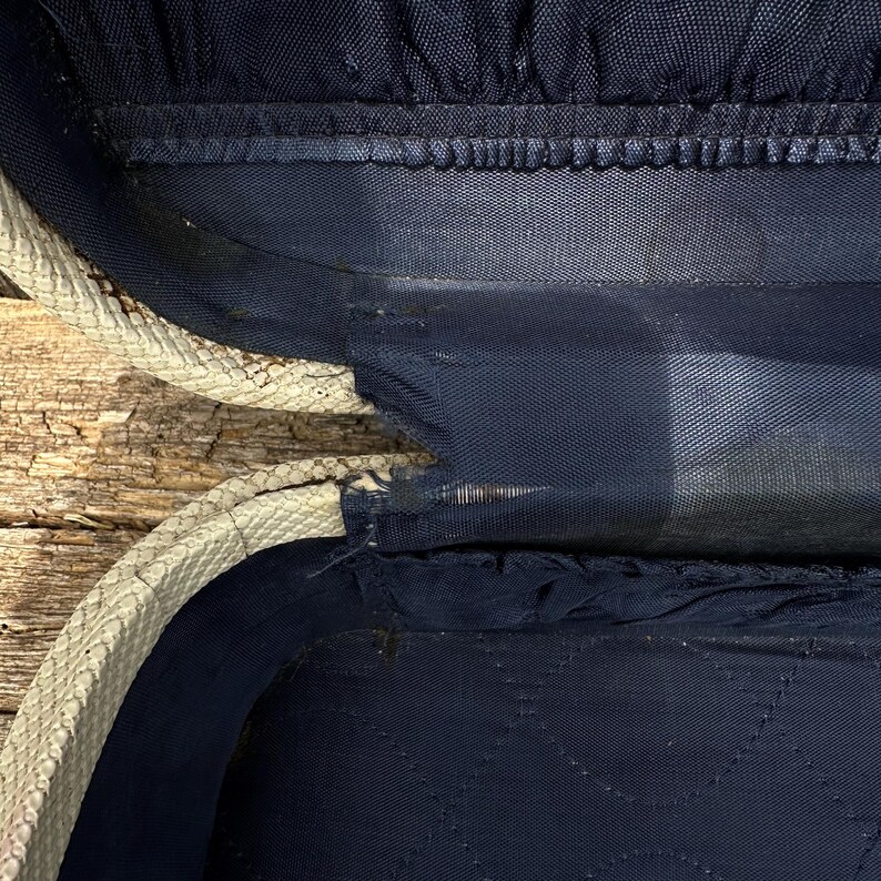 May include: Open view of a vintage suitcase interior. The interior is navy blue with a quilted pattern. The suitcase's edge is cream-colored with a textured pattern. The suitcase appears to be worn, with some visible wear and tear.
